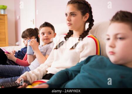 Brothers and sisters watching TV on living room sofa Stock Photo