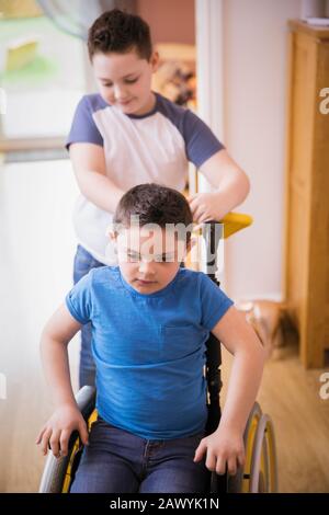 Boy pushing brother with Down Syndrome in wheelchair Stock Photo