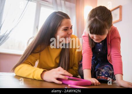 Happy sisters using digital tablet at table Stock Photo