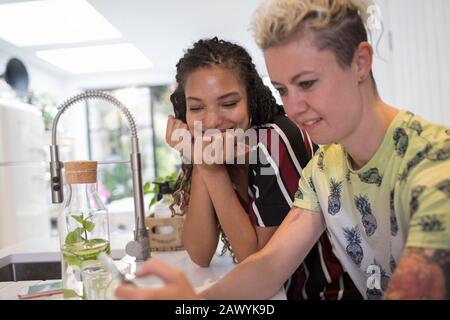 Young women friends using smart phone in kitchen Stock Photo