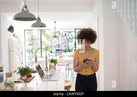 Young female freelancer using smart phone in kitchen Stock Photo