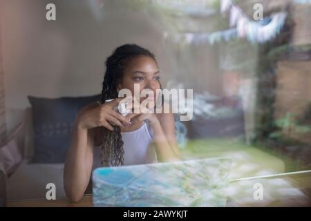 Thoughtful young woman drinking coffee at laptop in window Stock Photo