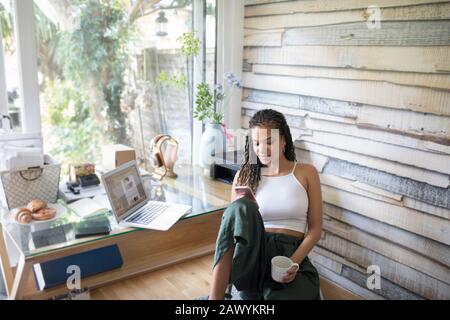Young woman with coffee using smart phone in home office Stock Photo