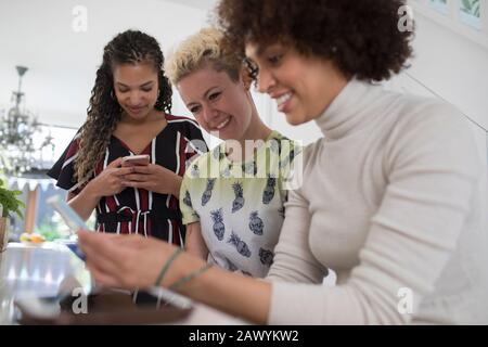 Young women friends using smart phones in kitchen Stock Photo