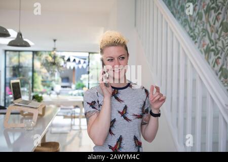 Smiling female freelancer talking on smart phone in kitchen Stock Photo
