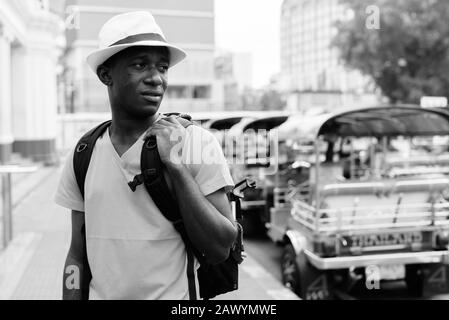 Young African tourist man thinking while holding backpack and sightseeing at railway station Stock Photo