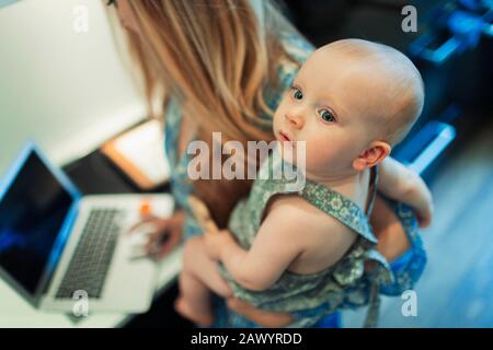 Mother working at laptop and holding cute baby daughter Stock Photo