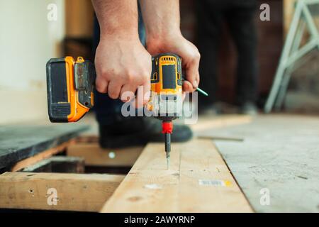 Close up construction worker using power drill installing floorboard Stock Photo