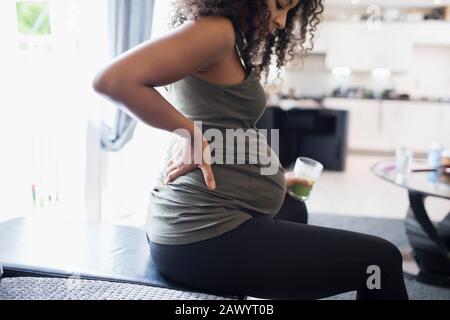 Young pregnant woman drinking green smoothie and holding back Stock Photo