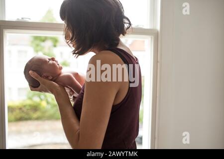 Mother cradling newborn baby son at window Stock Photo