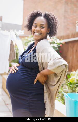 Portrait happy pregnant woman in sunny garden Stock Photo