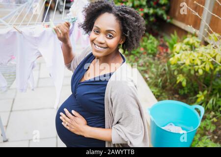 Portrait happy pregnant woman hanging laundry on clothesline Stock Photo