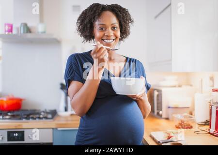 Portrait happy pregnant woman eating in kitchen Stock Photo