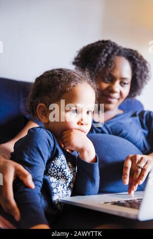 Pregnant mother and daughter using laptop Stock Photo