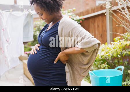 Happy pregnant woman hanging laundry on clothesline Stock Photo