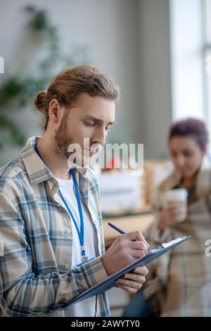 Young focused man with a badge standing and writing. Stock Photo