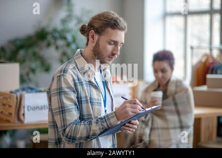 Young busy man standing indoors at work and writing. Stock Photo