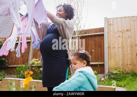 Pregnant woman with daughter hanging laundry on clothesline Stock Photo