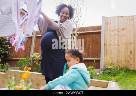 Happy pregnant woman with daughter hanging laundry on clothesline Stock Photo
