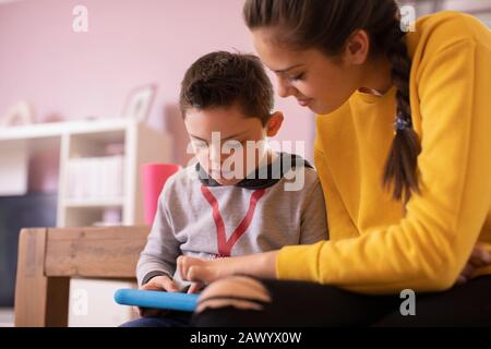 Sister helping brother with Down Syndrome using digital tablet Stock Photo