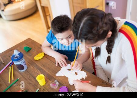 Girl helping brother with Down Syndrome color at table Stock Photo