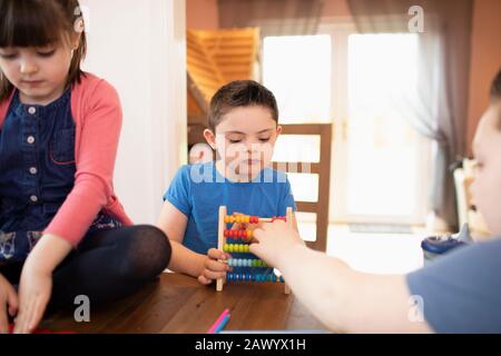 Boy with Down Syndrome and siblings playing with toy at table Stock Photo