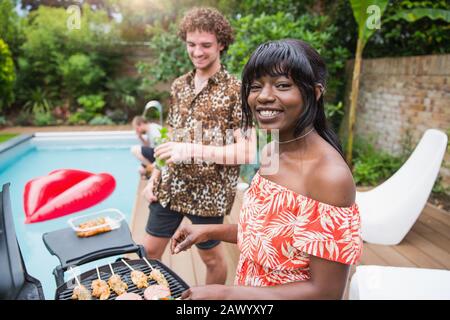 Portrait happy young multiethnic couple barbecuing at poolside Stock Photo