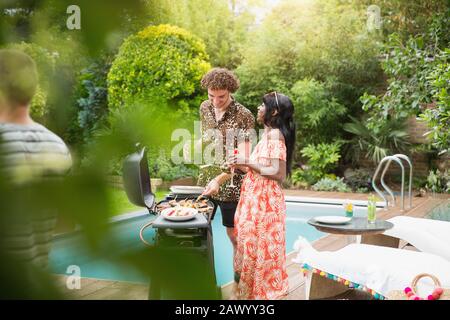 Young multiethnic couple barbecuing at summer poolside Stock Photo