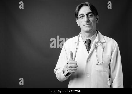 Mature handsome Italian man doctor against gray background Stock Photo