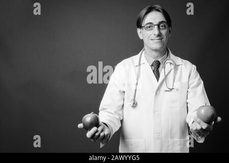 Mature handsome Italian man doctor against gray background Stock Photo