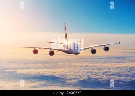 Shiny big plane in the sky above the clouds before sunset Stock Photo