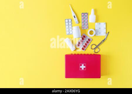 First aid kit red box with medical equipment and medications for emergency top view on pastel yellow background. Copy space. Stock Photo