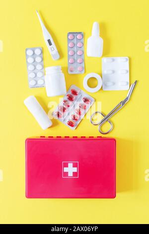 First aid kit red box with medical equipment and medications for emergency top view on pastel yellow background. Copy space. Stock Photo