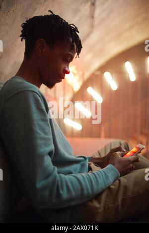 Side view portrait of modern African-American man using smartphone and smiling in futuristic interior, copy space Stock Photo