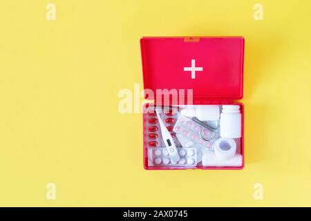 First aid kit red box with medical equipment and medications for emergency top view on pastel yellow background. Copy space. Stock Photo