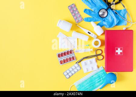 First aid kit red box with medical equipment and medications for emergency top view on pastel yellow background. Copy space. Stock Photo