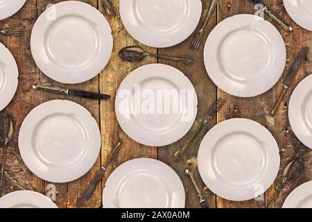 Pattern of vintage dinner plates, knives, forks and spoons on an old wooden table Stock Photo