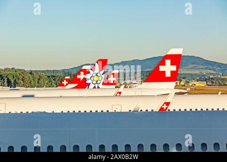 Zurich, Switzerland - June 11, 2017: Airport Zurich - tail fins of airplanes - airlines 'Swiss' and 'Edelweiss' planes in parking position, hill in ba Stock Photo