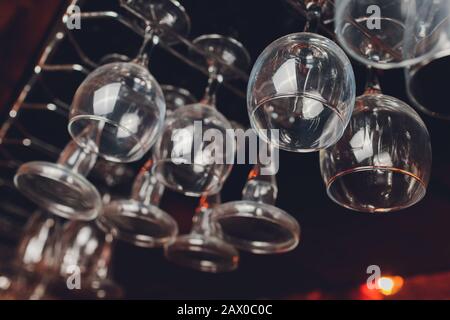 Closeup many upside down empty clear transparent crystal upturned wine glasses hanging in straight rows on brown wooden shelf, rack, showcase, stainle Stock Photo