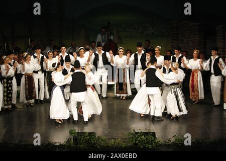 Professional dancers of the Banatul Folklore Ensemble hold hands in a traditional Romanian dance wearing traditional beautiful costumes. Stock Photo
