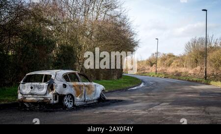 A burnt-out car left abandoned at the road side of a quiet rural location. Stock Photo