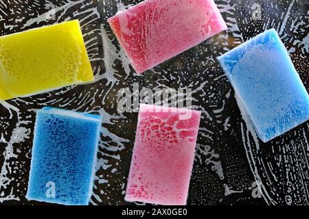 Multi-colored sponge for washing dishes on the glass with liquid and foam for washing dishes. Stock Photo