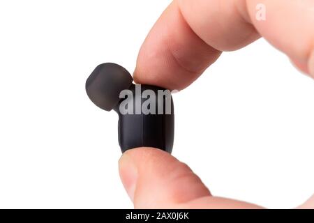 two caucasian fingers holding a black wireless earbud - close-up with selective focus, isolated on white background Stock Photo