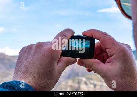 A man holding a GoPro camera taking a video of the mountain landscape during a hike Stock Photo