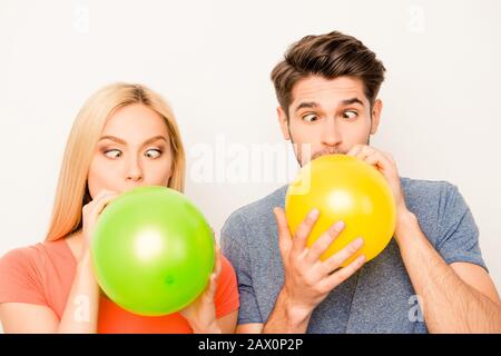 Two funny lovers inflating balloons for celebration and grimacing Stock Photo