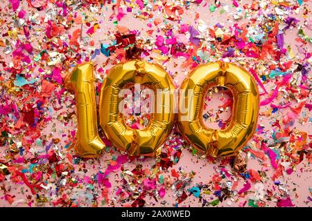 Number 100 gold birthday celebration balloon on a confetti glitter background Stock Photo