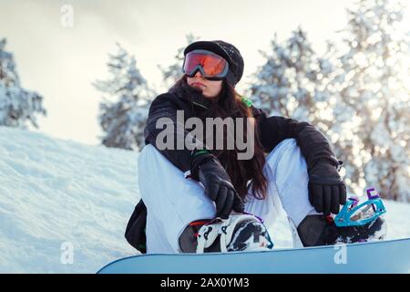 Stock photo of a young girl snowboarder is sitting on the snow of the mountain Stock Photo