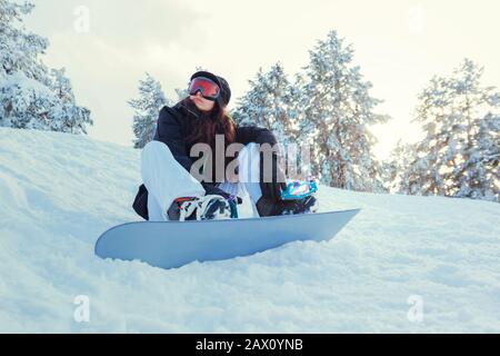 Stock photo of a young girl snowboarder who is sitting on the snow of the mountain Stock Photo