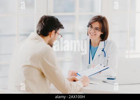 Woman doctor with stethoscope holds binder with patient personal medical card, consults patient who has medical problems, sit at hospital office, disc Stock Photo