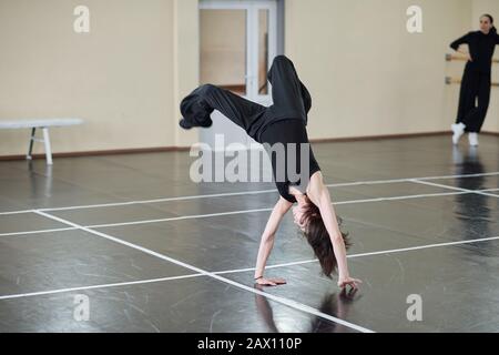 Young female dancer wearing black outfit doing difficult handspring element, horizontal shot Stock Photo